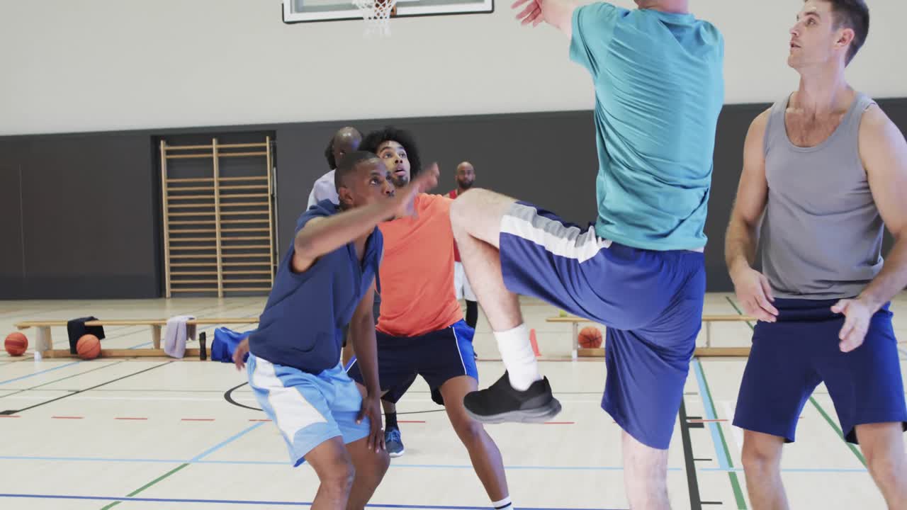 Diverse male basketball players blocking and shooting ball during game at indoor court, slow motion