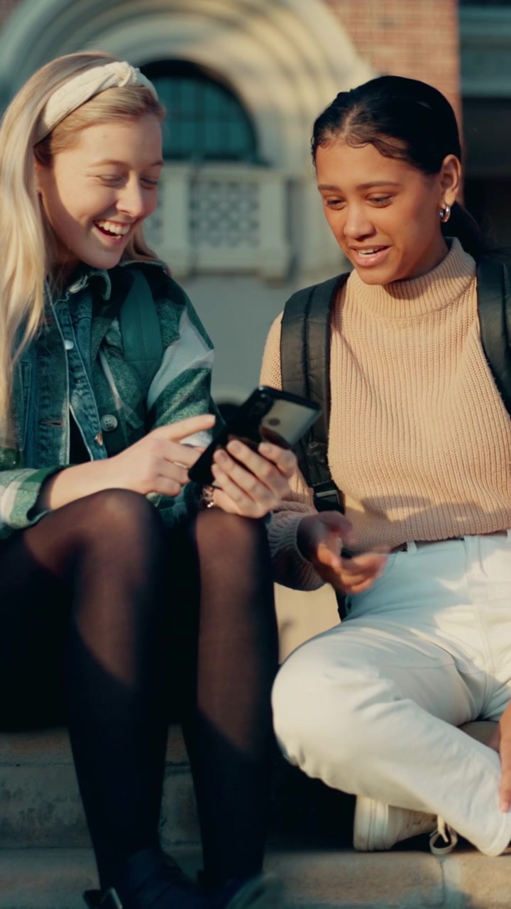 Two Female Students Sitting on Campus Steps Using a Smartphone