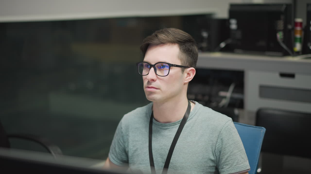 Focused individual working in office environment, using multiple computer monitors. Professional analyzing data or conducting technical tasks in modern workplace. Intense focus on work