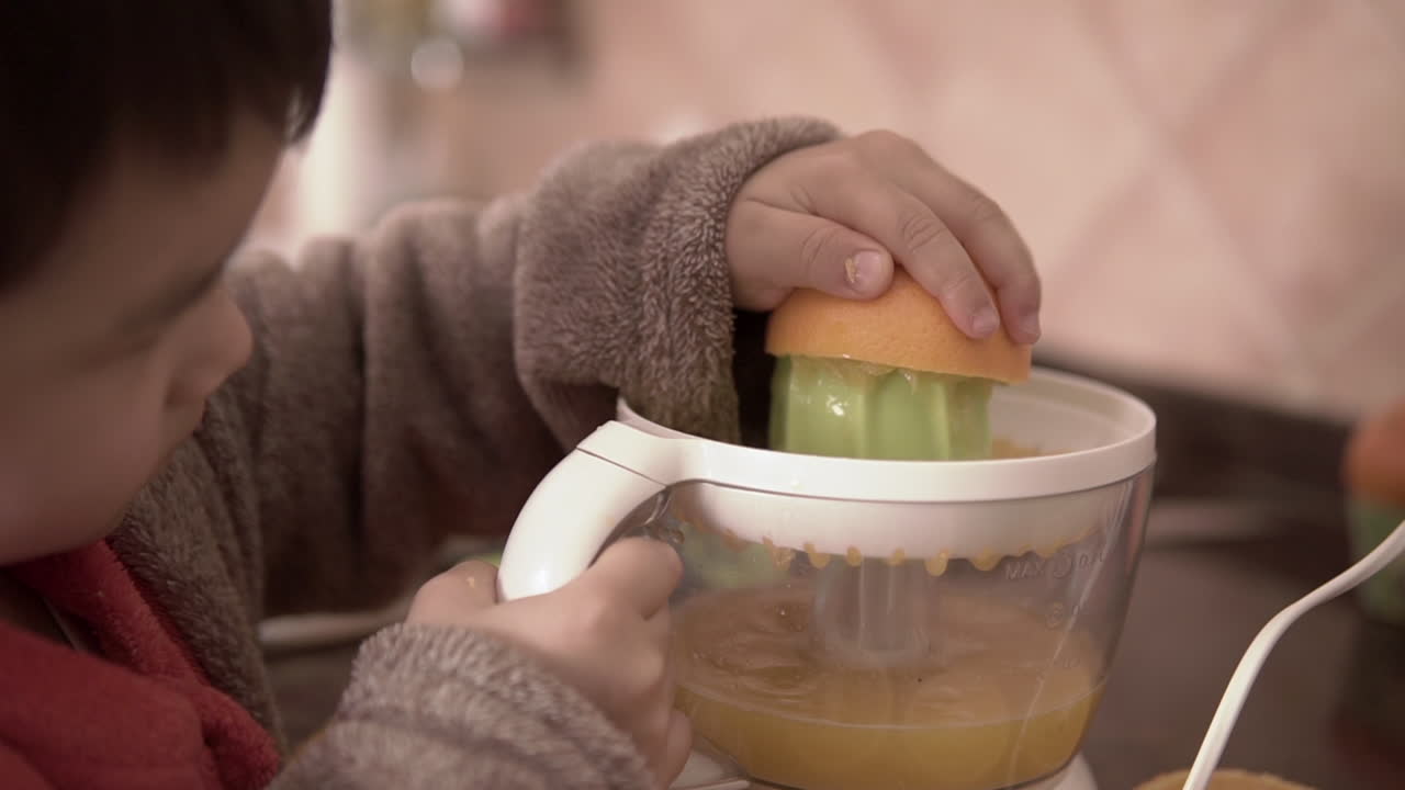 imágenes de primer plano en cámara lenta de un niño aprendiendo a hacer jugo de naranja fresco
