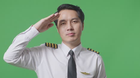 아시아 남성 조종사가 녹색 스크린 배경 스튜디오에 서서 경의를 표하고 인사를 하고 있습니다.