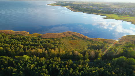 Aerial-trucking-shot-of-beautiful-Bay-of-Puck-with-green-shoreline,-golden-trees-and-small-city-in-background---Poland,Europe