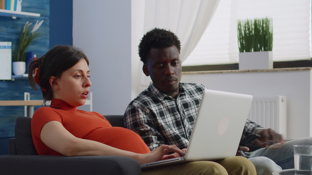 Interracial couple with pregnancy sitting together on couch