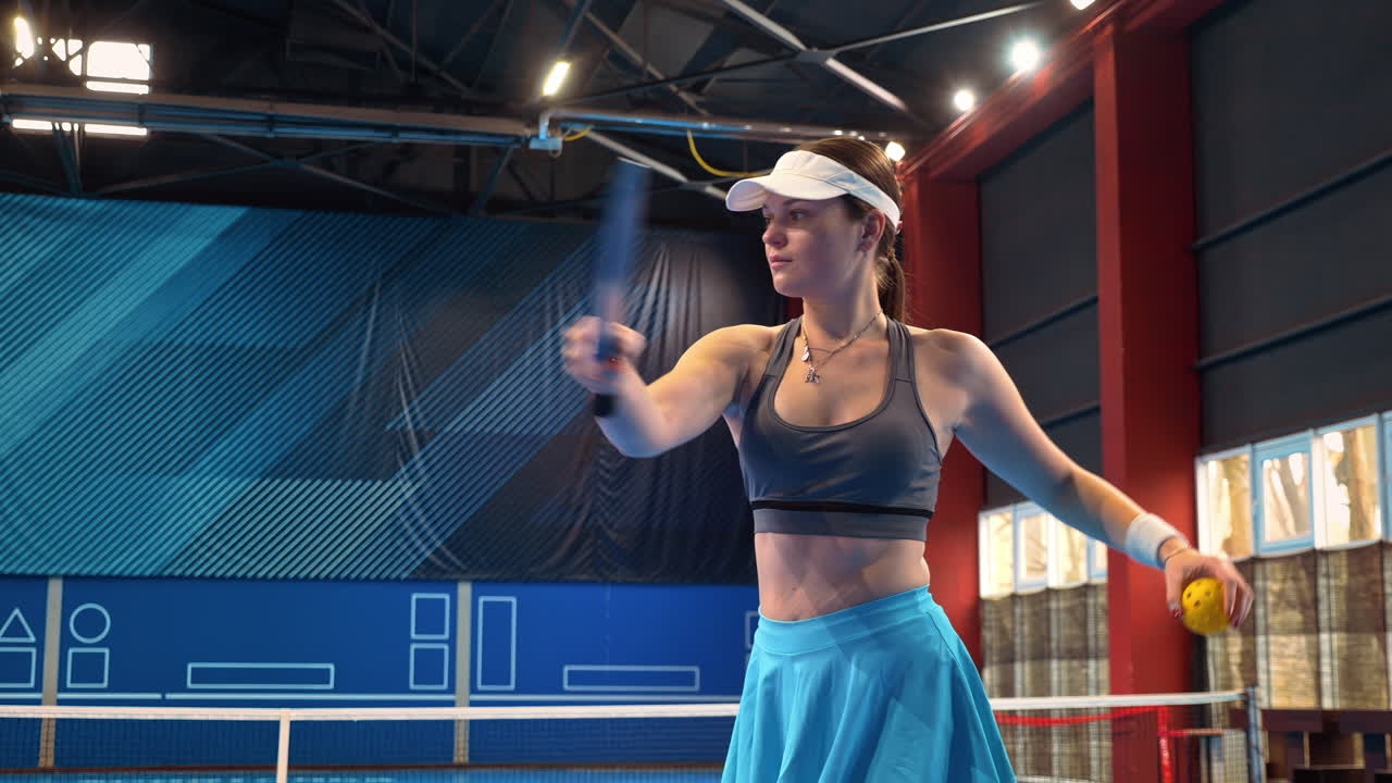 Woman in blue skirt warming up to play pickleball on a blue, inside court