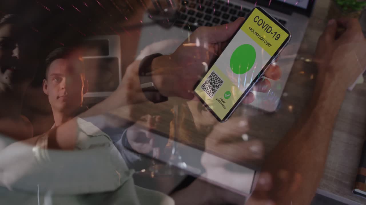 Animation of man holding smartphone with covid 19 vaccination passport over people having fun