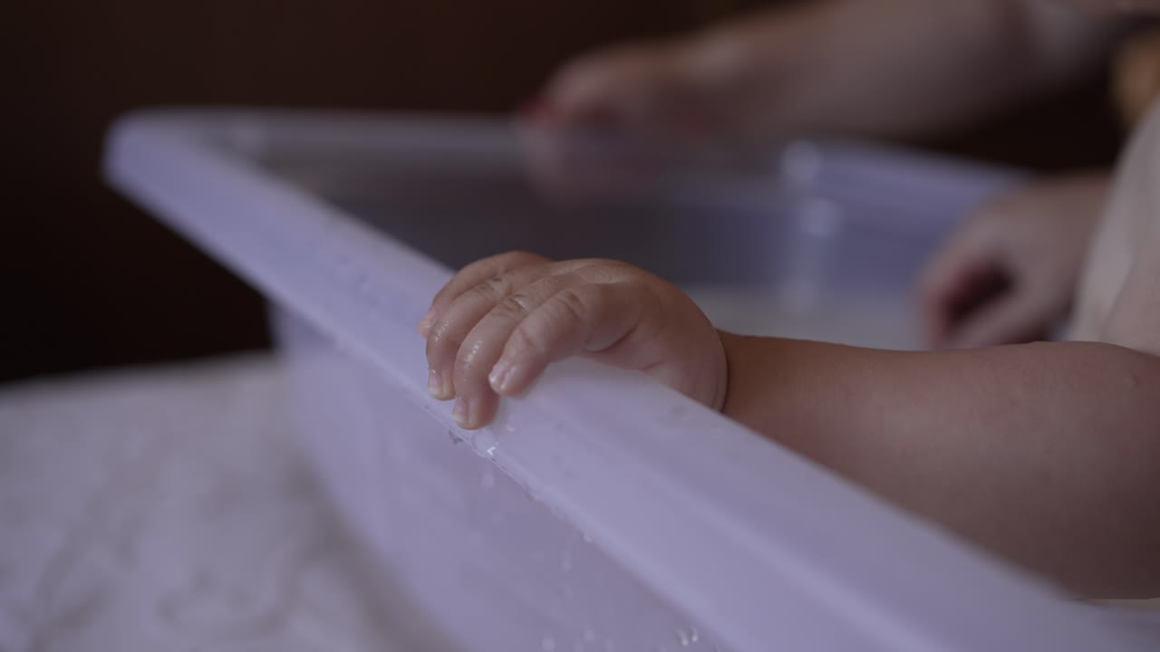 Close up of baby's hand resting on the edge of a plastic tub, capturing a tender and intimate moment