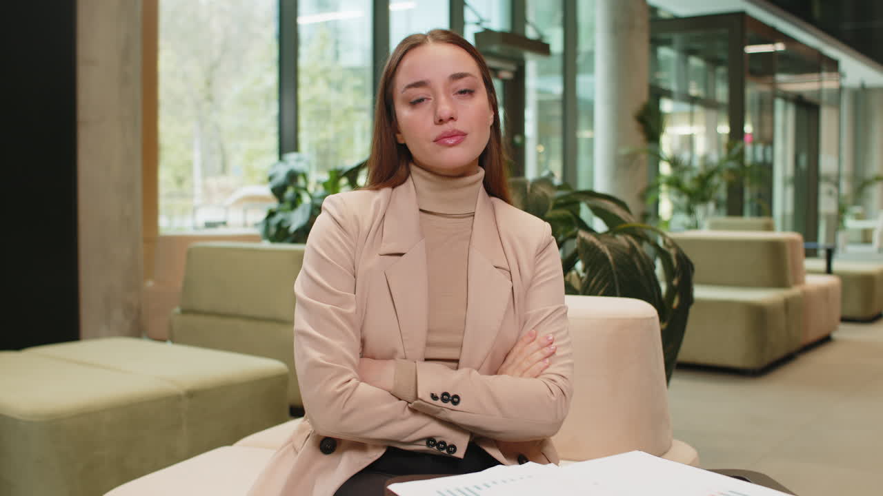 Portrait of upset caucasian businesswoman sitting in office lobby showing thumb down sign gesture