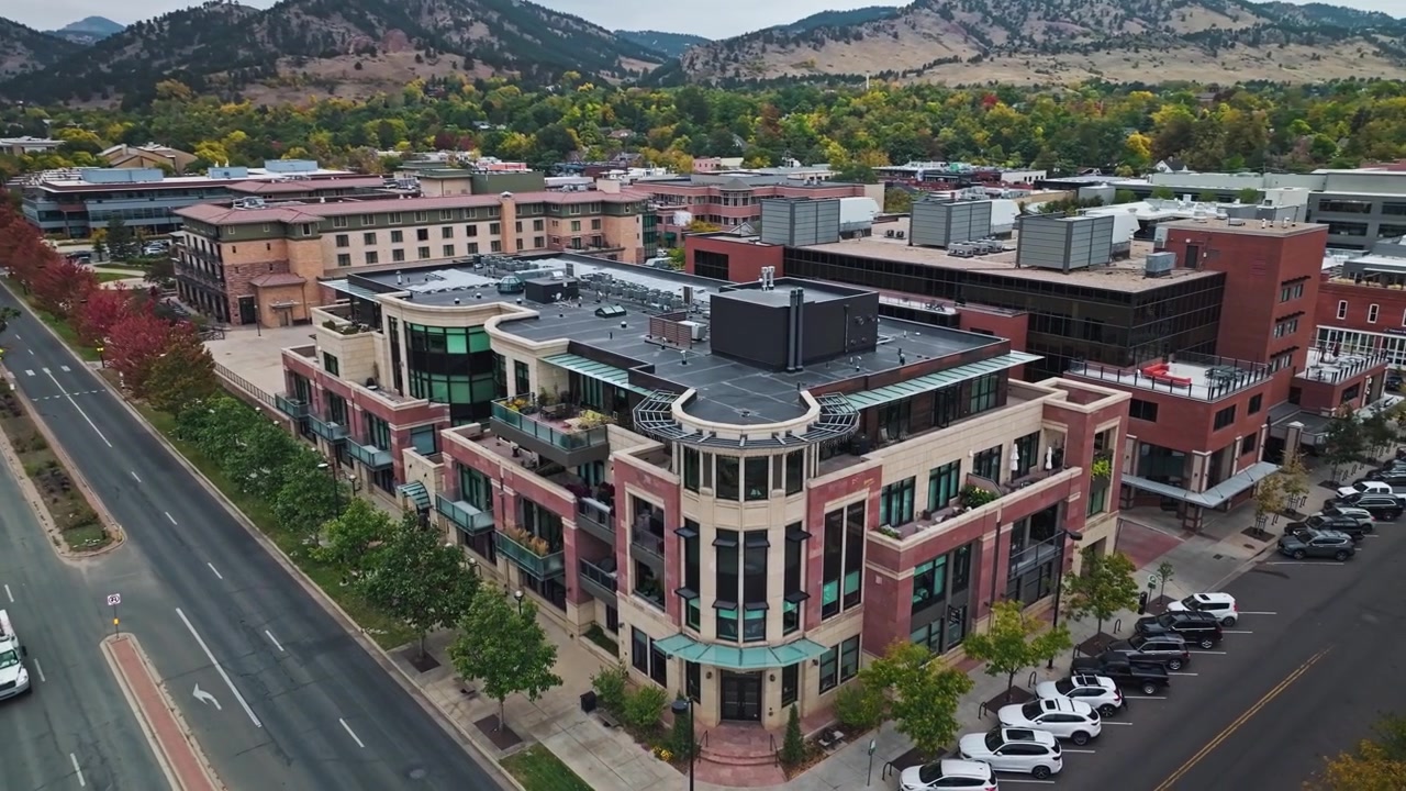 Droneopptak i en stigende sirkelbevegelse med klokken over Boulder sentrum og Flatirons, med fargerikt høstløv og forstadsområder
