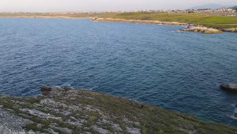 aerial view of rocky coastline while two people hiking on the edge of a cliff