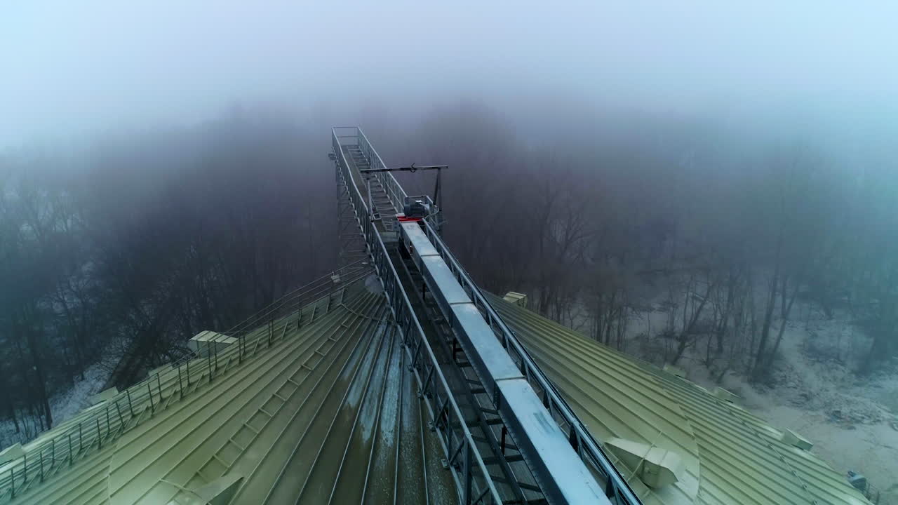 Big dirty rounded top of the granary tank. Flying along the metal support connecting the elevators. Top view on the winter foggy forest.
