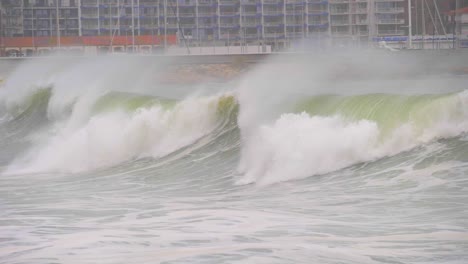 ola gigante en cámara súper lenta con el puerto deportivo al fondo rompiendo