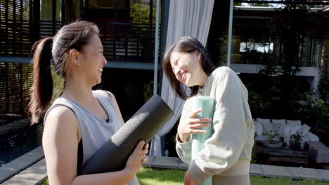 happy asian female friends with exercise mats laughing on sunny terrace, slow motion