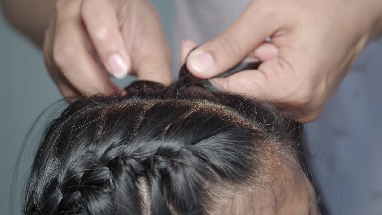 Primo piano di mani che intrecciano capelli neri intricati