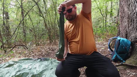 turista arrodillado en el suelo en un campamento en el bosque saca postes de una bolsa y comienza a ensamblarlos
