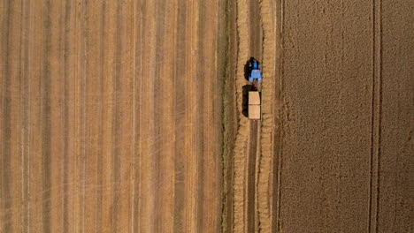 agriculture machinery and hay harvest, tractor in agricultural farmland field passing driving carry transporting hay bales, aerial top down view of farm work