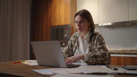 Mujer-De-Negocios-Madura-Que-Trabaja-Desde-Casa-Una-Mujer-Enfocada-Está-Trabajando-Con-Su-Computadora-Portátil-Y-Documentos-En-Papel-Sentados-En-La-Cocina-De-Su-Casa.-Aplicación-Para-Computadora-Portátil-Calcular-Costos-Gastos-Estimar-El-Presupuesto-Para-El-Proyecto