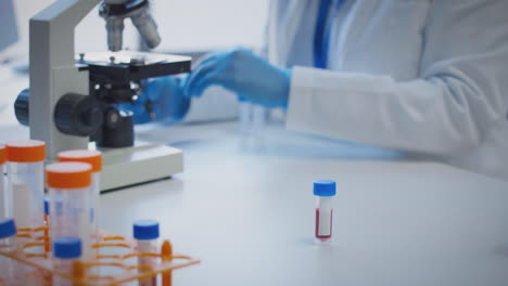 primer plano de un trabajador de laboratorio que realiza investigaciones utilizando un microscopio con una muestra de sangre con una etiqueta en blanco