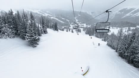 pov empty chairlift over ski slope with big pine trees at ski resort during winter