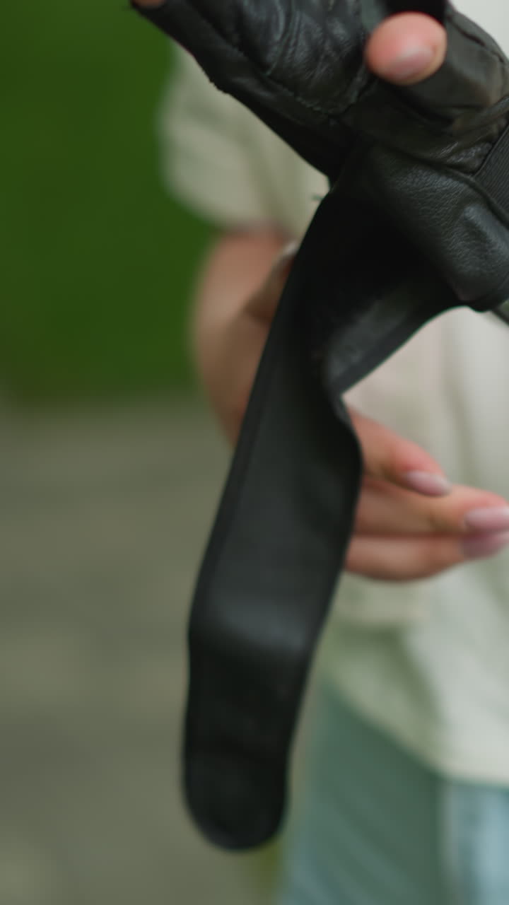 primer plano de una mujer joven que se pone guantes negros con el enfoque en sus manos y reloj inteligente en la muñeca derecha, el fondo presenta vegetación borrosa y pistas de camino al aire libre