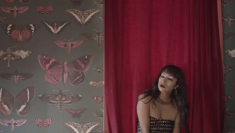 A-tracking-shot-of-a-beautiful-woman-wearing-a-tube-top-while-dancing-sensually-in-front-of-a-red-curtain-hanging-on-a-wall-of-various-butterfly-photographs