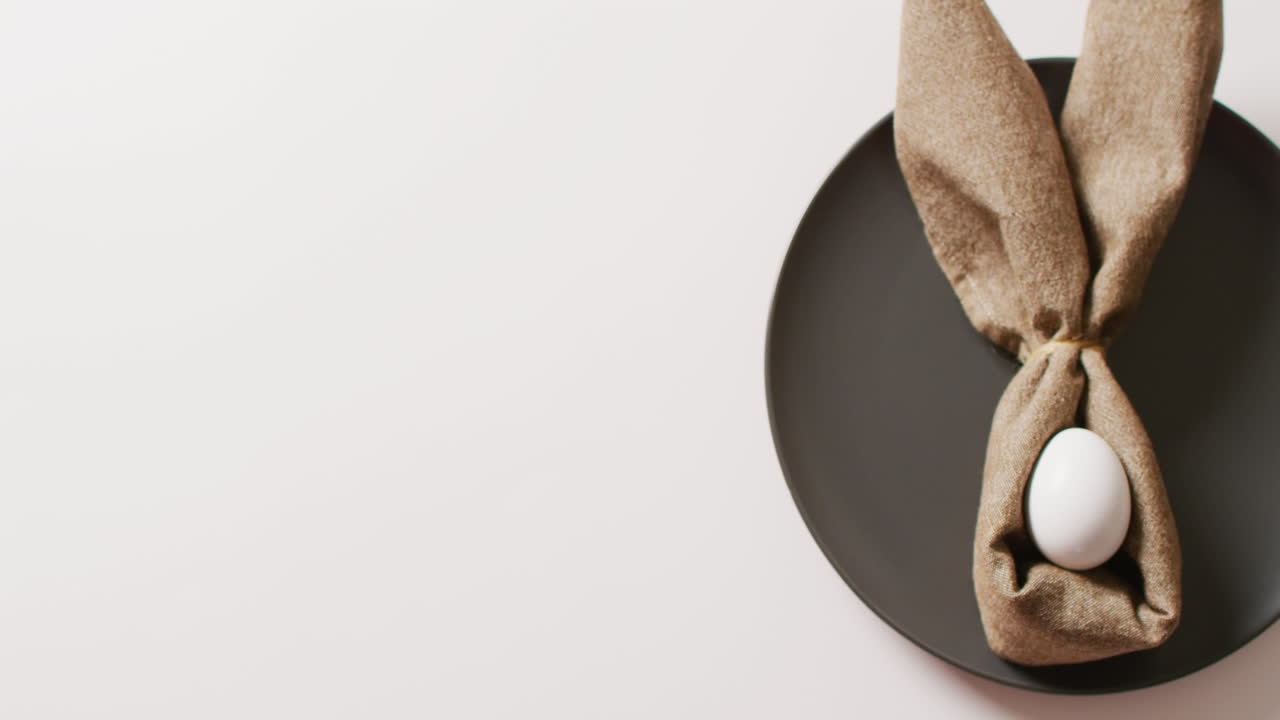 Egg and ribbon in shape of rabbit on plate on white background with copy space