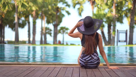 Hermosa-Mujer-De-Pelo-Largo-Se-Sienta-Al-Borde-De-La-Piscina-Con-Traje-De-Baño-Y-Sombrero