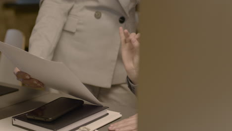 close up of two female employees talking together and checking printed business reports in the office