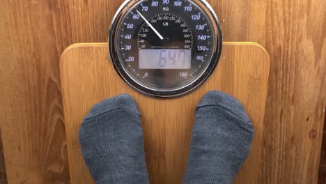 man wearing grey sock step on digital scales to check his weight.