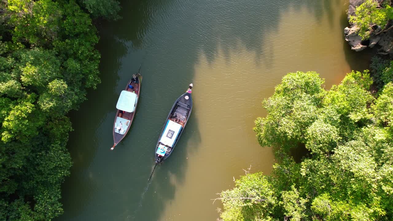 un dron aéreo de arriba hacia abajo de dos botes tailandeses de madera se cruzan en el río rodeados de bosques de manglares en la ciudad de krabi, tailandia, durante una tarde de puesta de sol