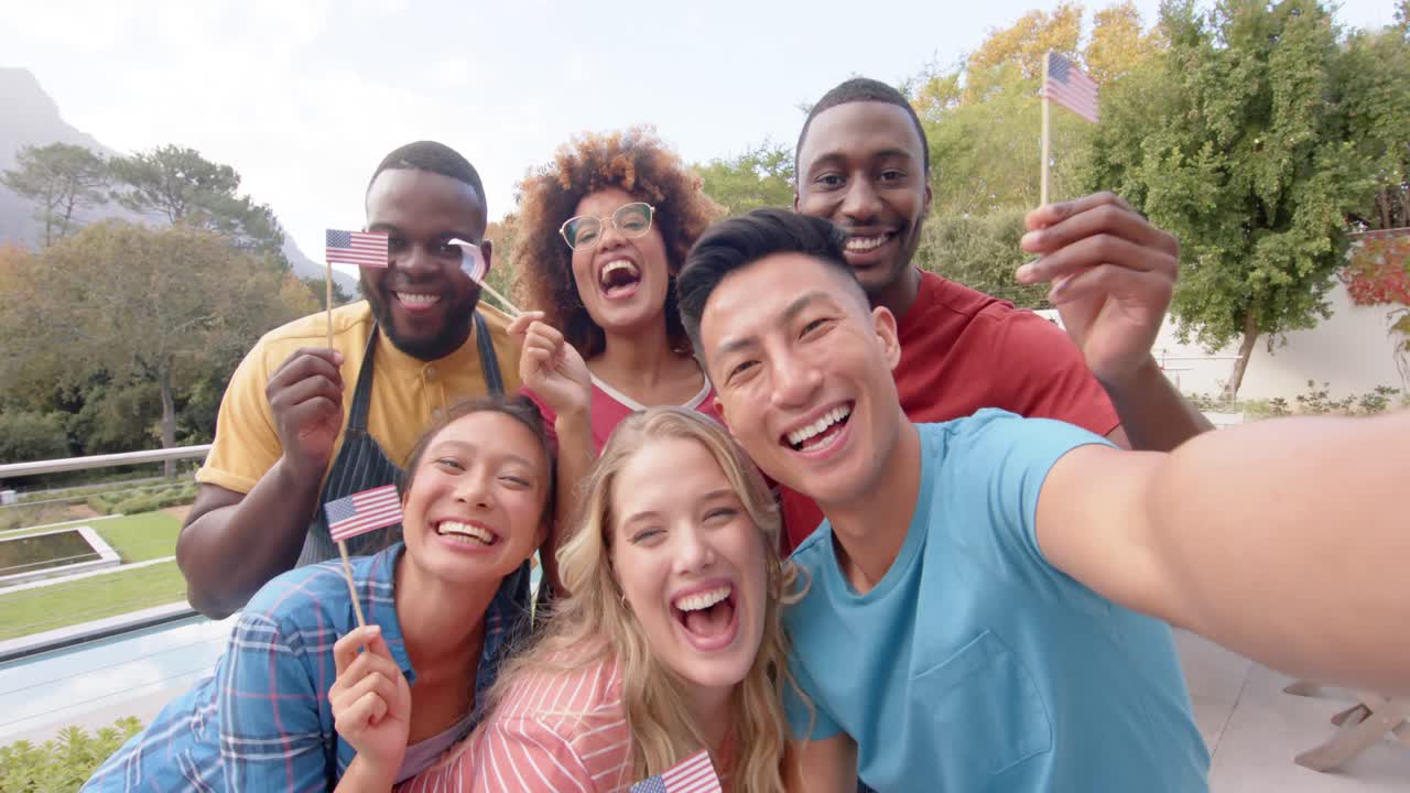 Grupo feliz e diverso de amigos segurando bandeiras dos EUA e tirando selfie no jardim, em câmera lenta