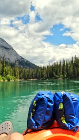 vertical pov captures a kayaker drifting leisurely along the bow river. the gentle current carries them through emerald waters, framed by towering forest and the breathtaking canadian rockies.