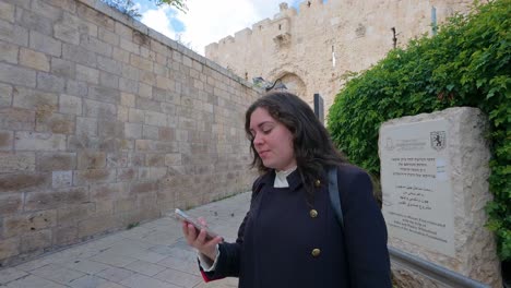 young adult woman talking on phone near jerusalem old city walls, zion gate. slow motion.
