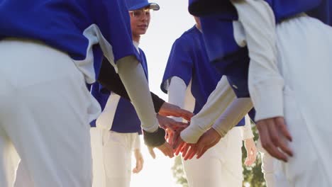 diverse group of female baseball players on sunny pitch, in a huddle, stacking hands