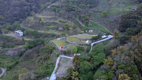 Serpentine-mountain-roads-with-lush-greenery-and-a-single-red-car,-daytime,-aerial-view