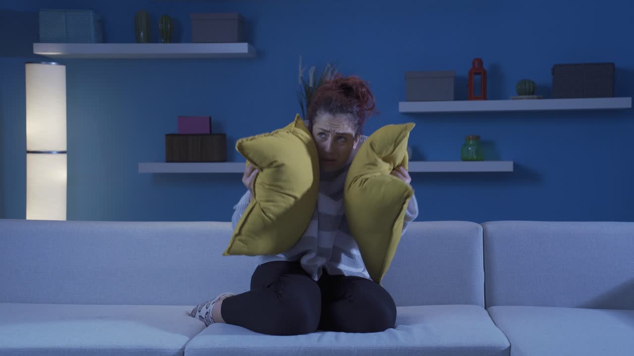 The woman who presses the pillows on her head with fear.