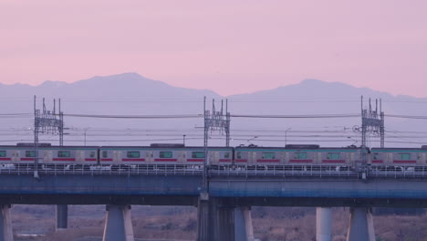 train passing by on railway bridge at dusk in tokyo japan with majestic mountain in background