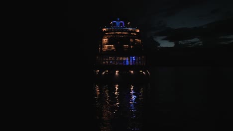 shot of back of luxury cruise ship sailing along the bay past the coastline on a dark night