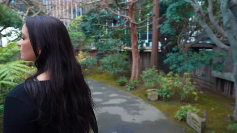 a 4k slow-motion, stabilized video depicting a beautiful young middle eastern female model exploring a lush japanese tea garden walking along a garden path, peninsula, california