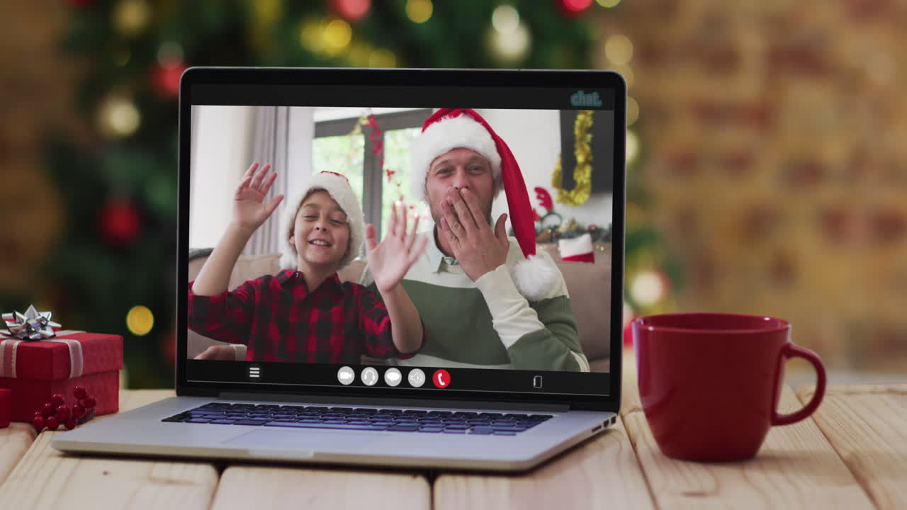 padre y hijo felices saludando en una videollamada en una computadora portátil, con decoraciones de navidad y árbol