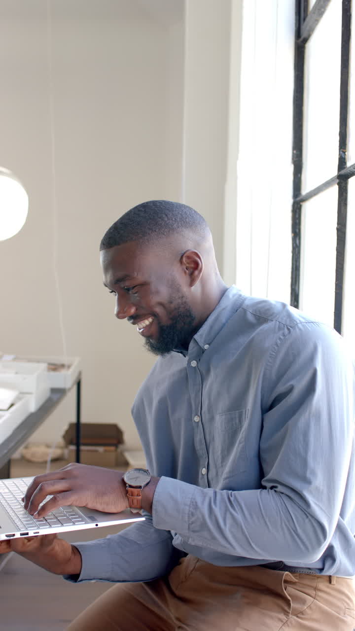Vertical video: Smiling businessman typing on laptop while sitting at desk in office