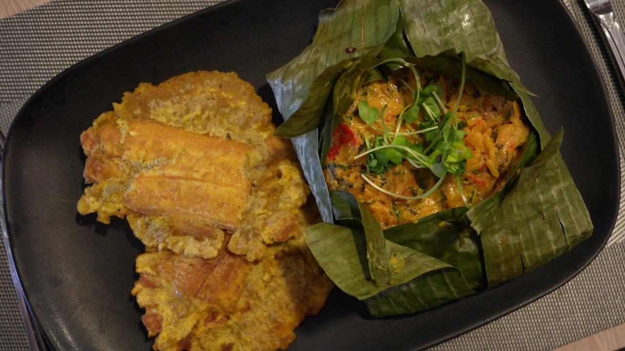 Foto close-up detail fiambre, hidangan Amerika Latin yang semarak, disajikan di daun pisang dengan pisang goreng keemasan di piring hitam, di bawah pencahayaan dalam ruangan yang hangat untuk tampilan gourmet yang menggugah selera.