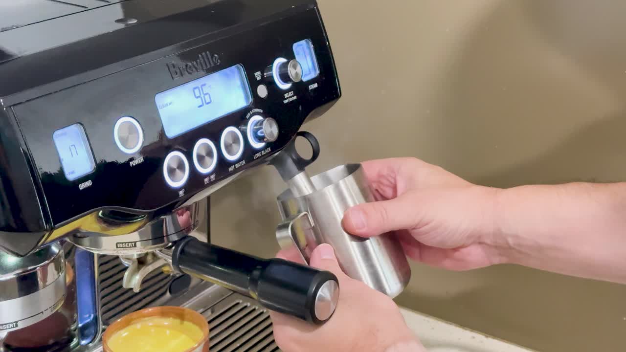 Hands using a coffee machine to froth milk in a cozy kitchen setting with warm lighting