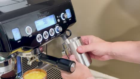 hands using a coffee machine to froth milk in a cozy kitchen setting with warm lighting