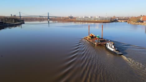 Aerial-view-of-tugboat-pushing-barge-down-the-Maumee-River,-in-downtown-Toledo,-Ohio,-USA