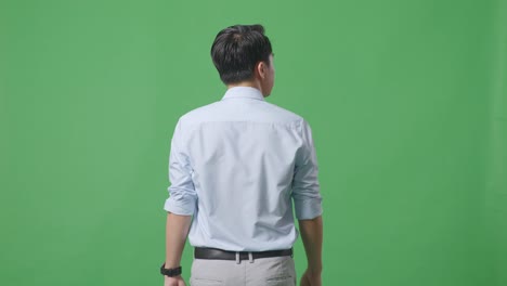 back view of asian business man walking and looking around on green screen background in the studio