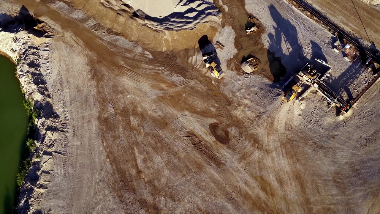 Drone aerial footage shows wheel loaders operating at a busy aggregate gravel and sand pit, moving raw materials under bright sunlight. Static, straight down view.