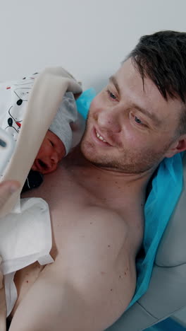 caucasian bearded male takes selfie of himself and of a child lying on the chest. newborn is placed on dad's chest for skin to skin contact. vertical video