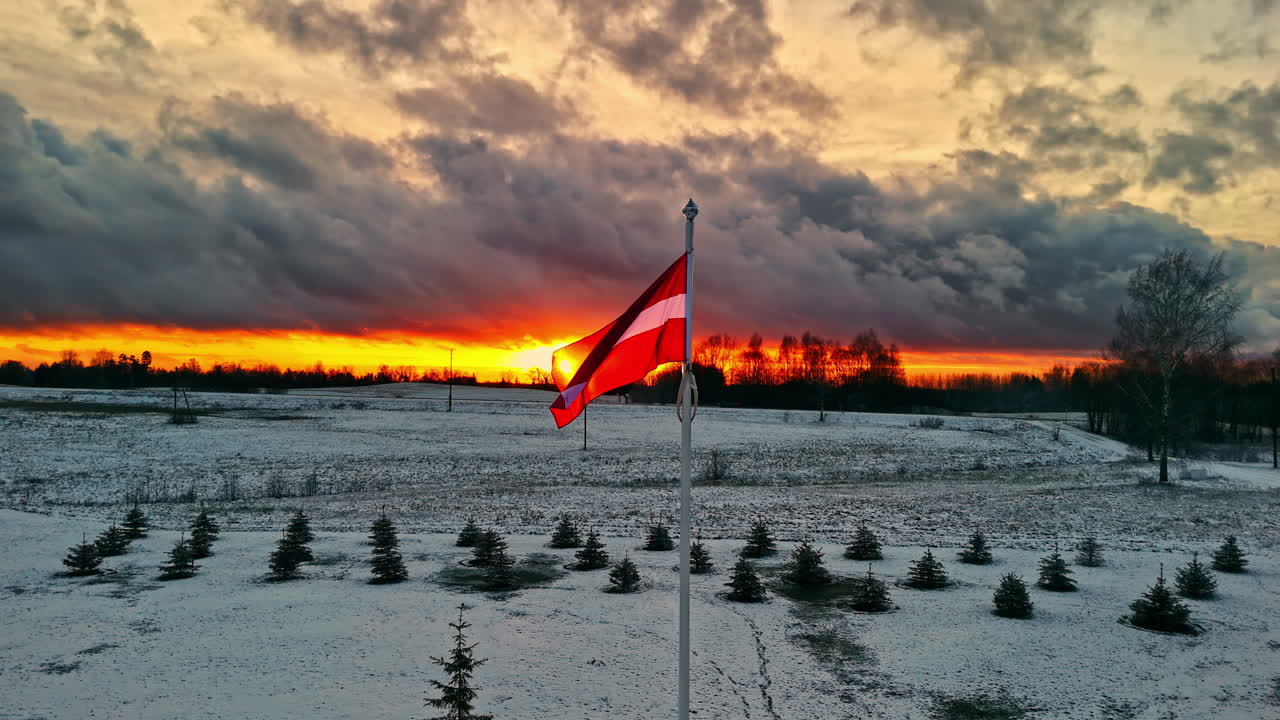 Latvian flag waving in snowy field at sunset, Cesis, Latvia, national pride