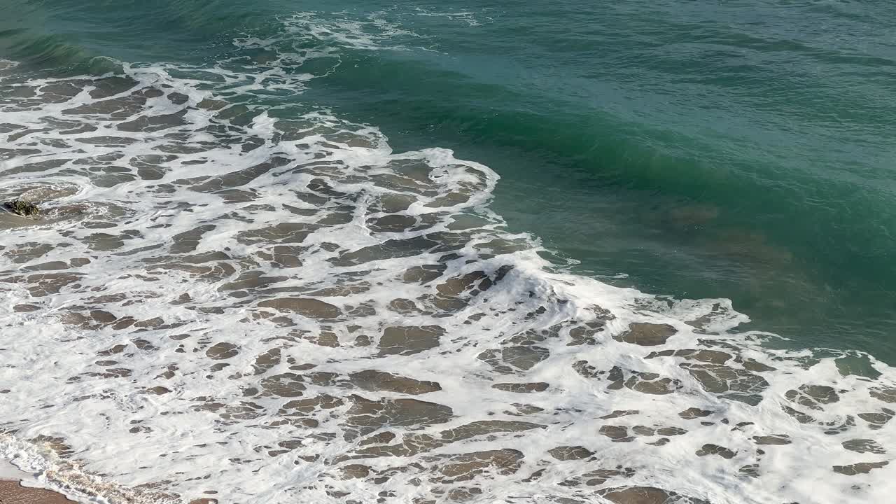 Ripresa statica di onde oceaniche turchesi che si infrangono su una spiaggia sabbiosa con schiuma di mare bianca e superficie dell'acqua testurizzata