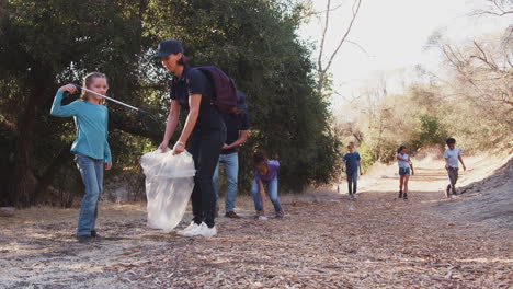 adult team leaders with group of children at outdoor activity camp collecting litter together